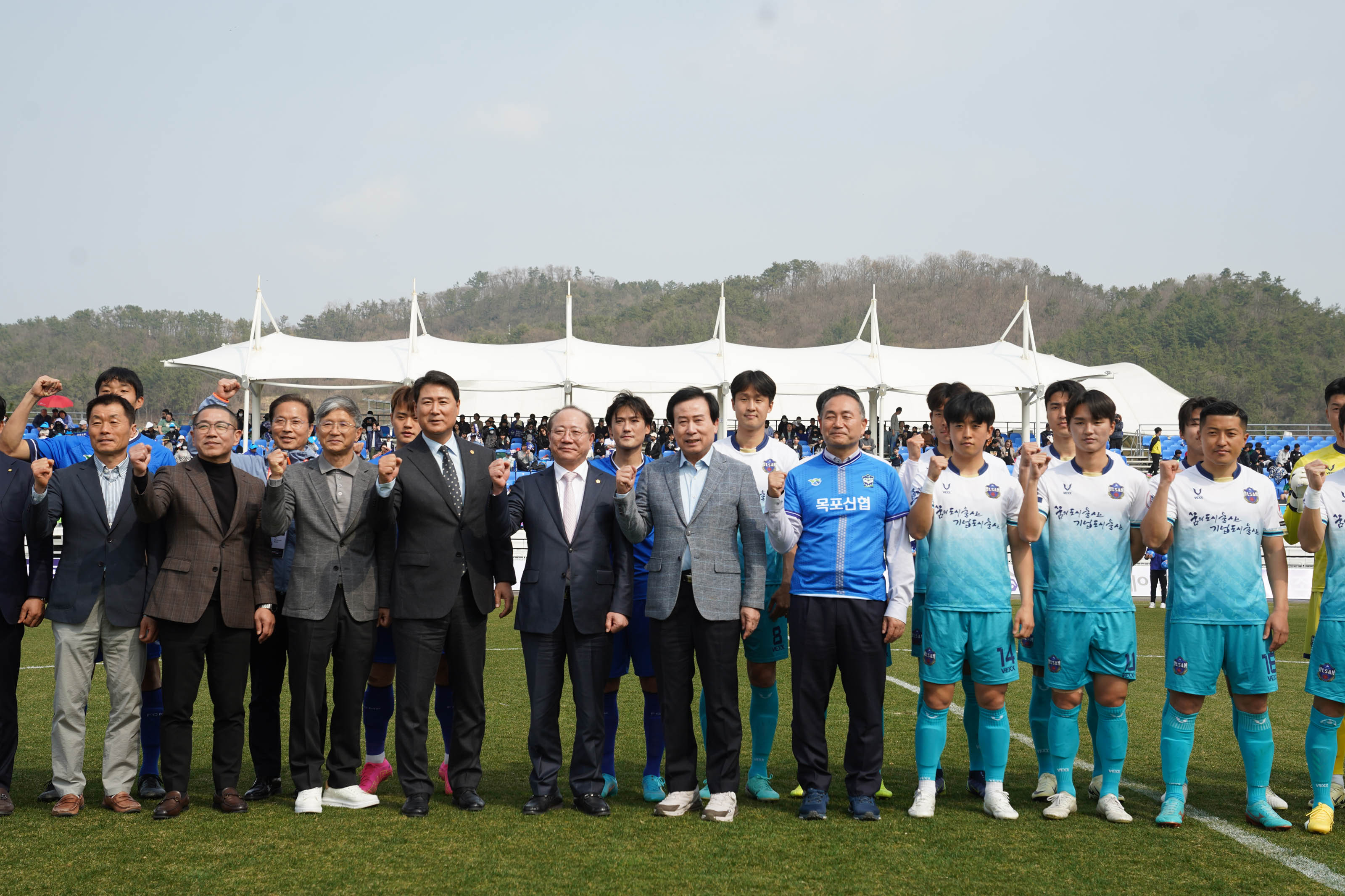 파란색 유니폼의 선수들과 민트색과 하얀색이 섞인 유니폼을 입은 선수들과 함께 박홍률 시장을 중심으로 정장을 입은 6여명의 사람들이 가로로 두 줄로 서서 화이팅을 외치는 사진