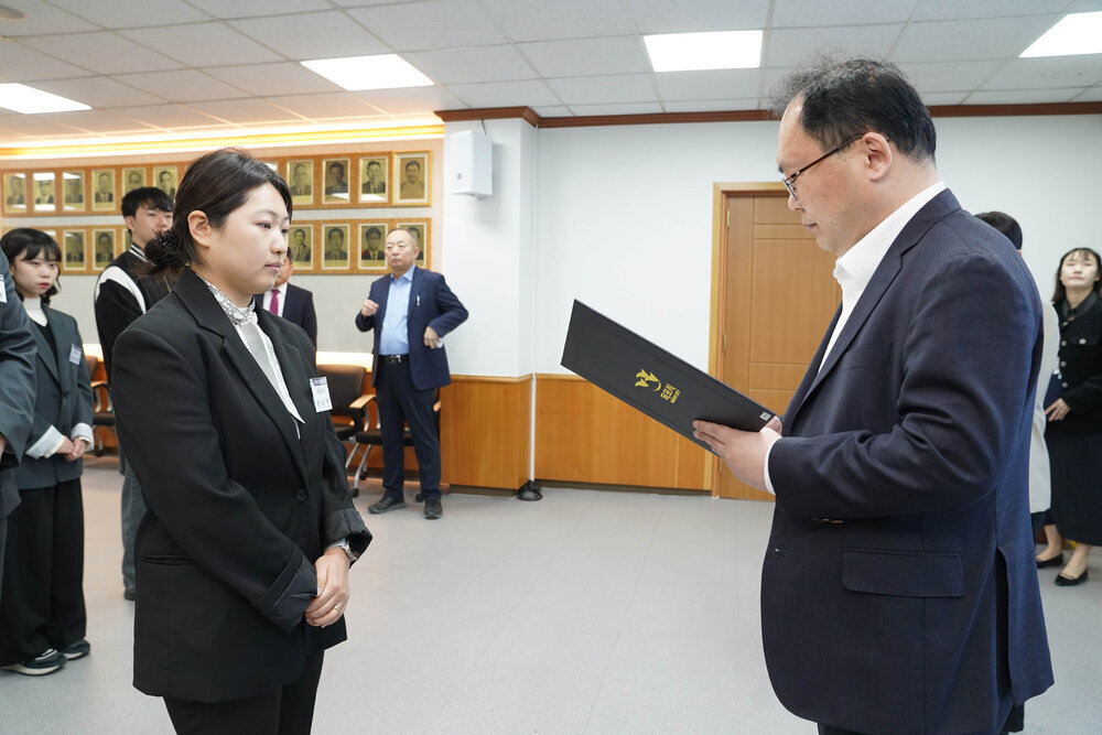 신규자 임용식에서 정장을 입은 남성이 검정 정장을 입은 여성 직원에게 임용장을 전달하는 모습