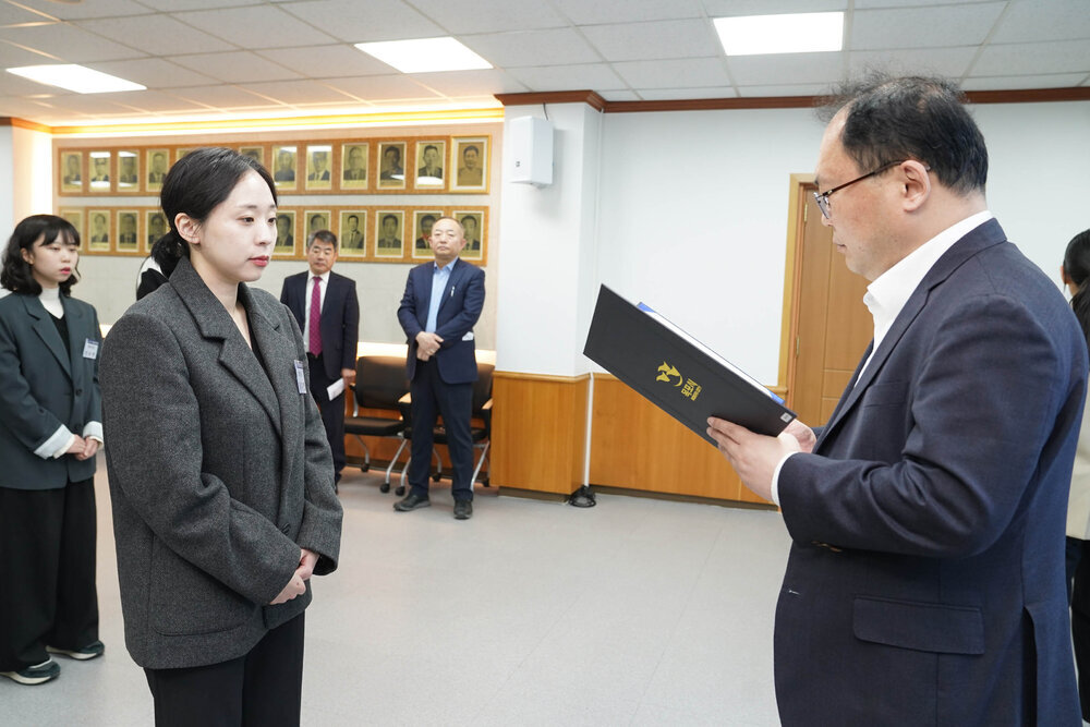 신규자 임용식에서 정장을 입은 남성이 회색 재킷을 입은 여성 직원에게 임용장을 전달하는 모습