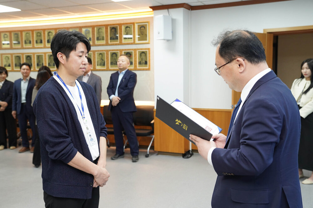 수시인사 임용장 수여식에서 정장을 입은 남성이 네이비 니트 카디건을 입은 남성 직원에게 임용장을 전달하는 모습