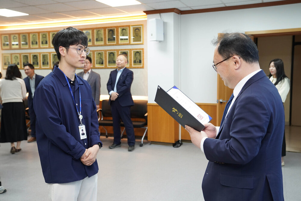 수시인사 임용장 수여식에서 정장을 입은 남성이 남색 셔츠를 입은 안경 쓴 남성 직원에게 임용장을 전달하는 모습