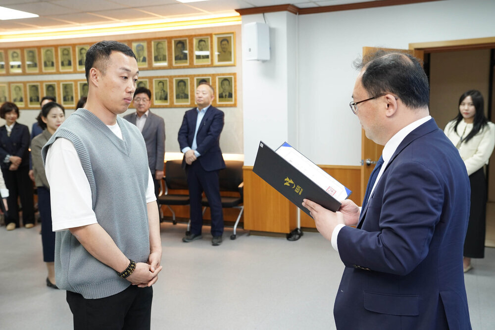 수시인사 임용장 수여식에서 정장을 입은 남성이 회색 니트 조끼를 입은 남성 직원에게 임용장을 전달하는 모습