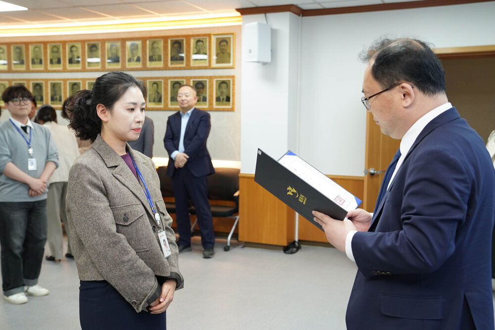 수시인사 임용장 수여식에서 정장을 입은 남성이 갈색 재킷을 입은 여성 직원에게 임용장을 전달하는 모습