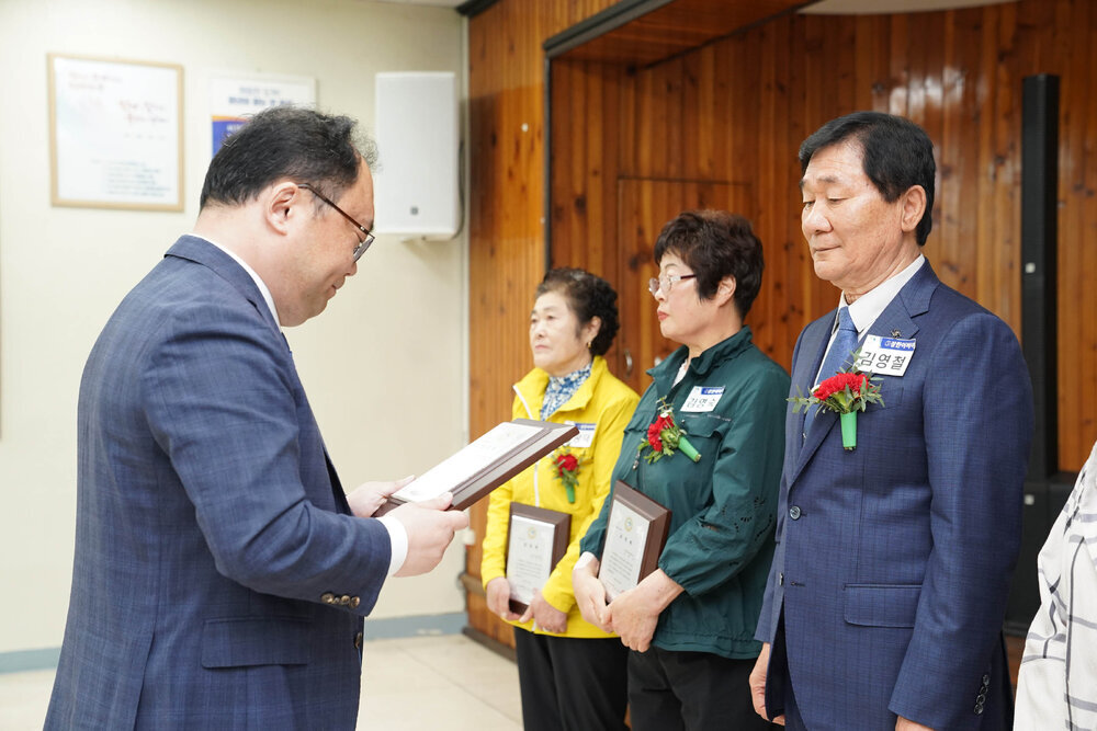 정장을 입고 안경을 낀 남성이 남색 정장을 입은 김영철에게 패를 수여하고 있다