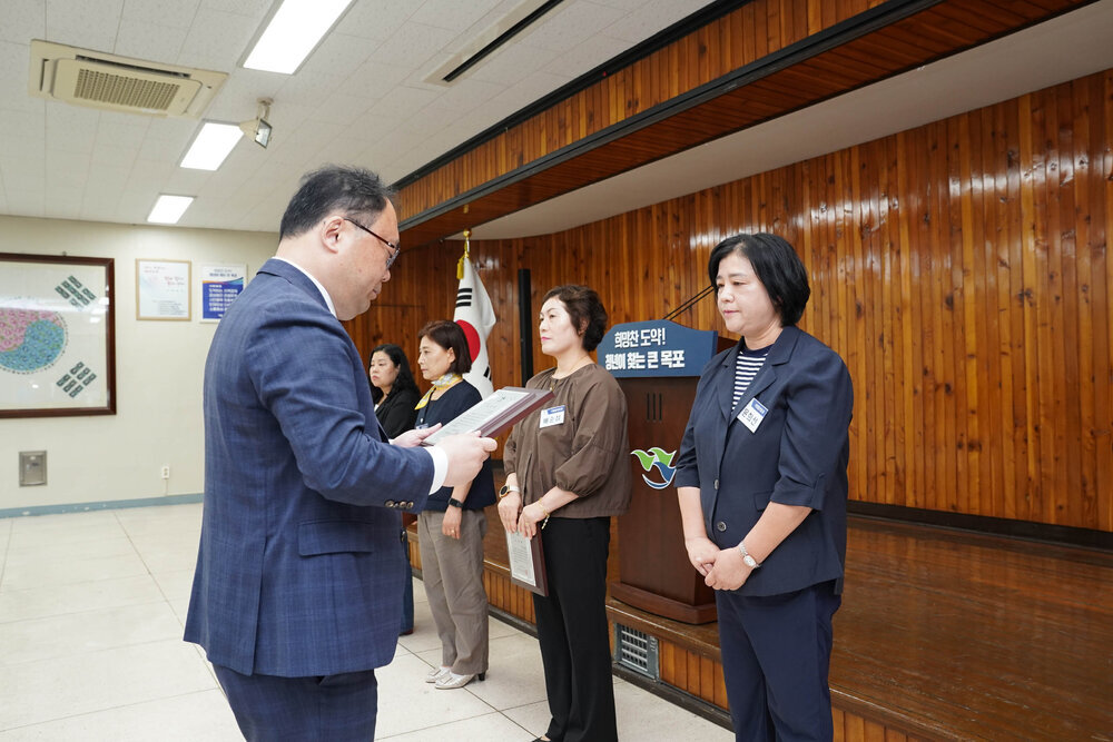 정장을 입고 안경을 낀 남성이 줄무늬 티에 5부 남색 자켓을 입은 여성에게 패를 수여하고 있다