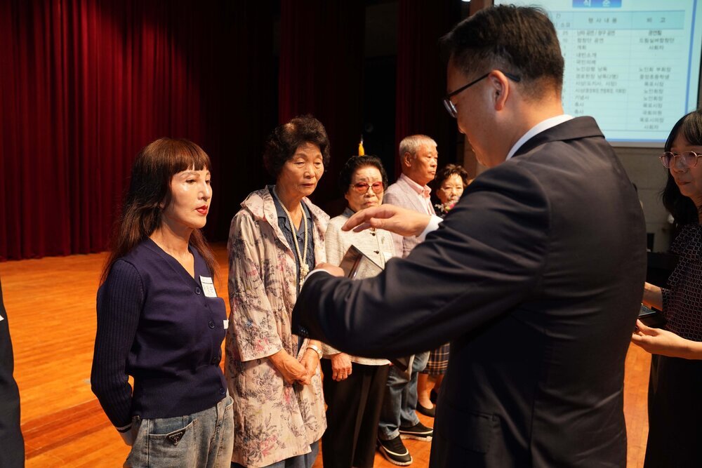 정장 차림의 관계자가 남색 상의를 입은 여성 수상자에게 패를 전달하기 위해 준비하는 모습이다.