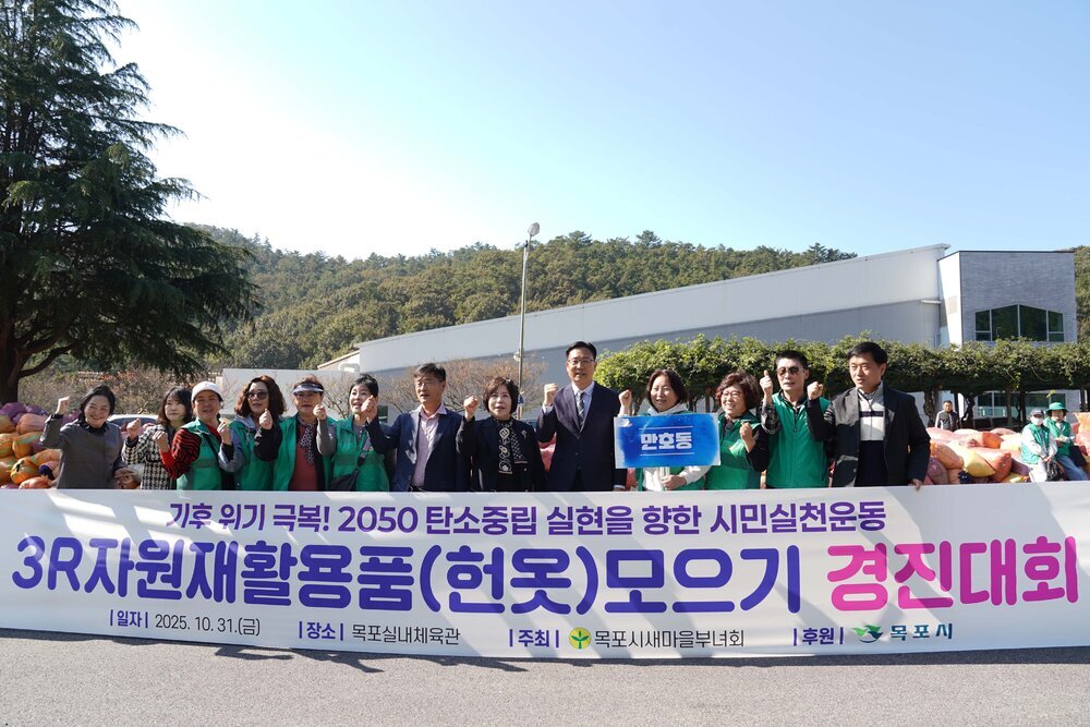'3R 자원재활용품(헌옷) 모으기 경진대회' 현수막을 들고 만호동 참가자들이 파이팅 포즈를 취하고 있다. 현수막에는 '기후 위기 극복! 2050 탄소중립 실현을 향한 시민실천운동', 일시 2025. 10. 31.(금), 장소 목포실내체육관, 주최 목포시새마을부녀회, 후원 목포시 문구가 적혀 있다.