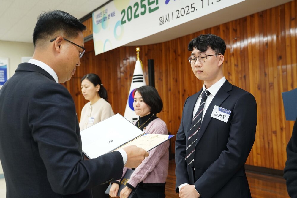 11월 정례조회로 정장을 입고 안경을 쓴 남성이 흰색 와이셔츠에 사선줄무늬 넥타이를 하고 검은색 정장을 입은 송현우 수상자에게 상장을 수여 하고 있다.