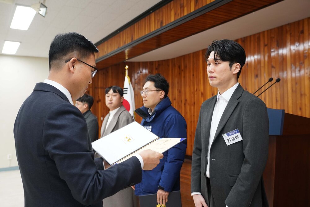 2월 정례조회에 정장을 입고 안경을 낀 남성이 흰색 셔츠에 검은색 정장 자켓을 입은 권재혁에게 패를 수여하고 있다.