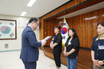 정장을 입고 안경을 낀 남성이 청바지에 검은색 자켓을 입은 여성에게 패를 수여하고 있다