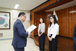 정장을 입고 안경을 낀 남성이 뿔테안경을 끼고 흰색 셔츠를 입은 여성에게 상장을 수여하고 있다