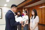 정장 차림의 관계자가 연베이지색 원피스를 입은 여성 수상자에게 패를 전달하며 읽고 있는 모습이다.