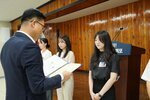 정장 차림의 관계자가 검은색 반팔 블라우스를 입은 여성 수상자에게 패를 전달하며 읽고 있는 모습이다.