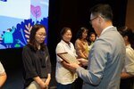 정장 차림의 관계자가 검은색 상의를 입은 여성 수상자에게 패를 전달하며 읽고 있는 모습이다.