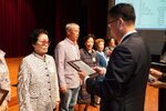 정장 차림의 관계자가 안경을 쓴 여성 수상자에게 패를 전달하며 읽고 있는 모습이다.