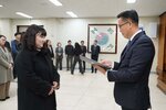 2026년 상반기 4급이하 정기인사로 정장을 입은 남성이 실내 행사장에서 한 여성에게 상장을 전달하며 내용을 읽고 있고, 여성은 검은색 코트를 입고 두 손을 모은 상태로 서 있으며 뒤쪽으로 참석자들이 줄지어 서서 행사를 지켜보고 있다.