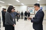 2026년 상반기 4급이하 정기인사로 정장을 입은 남성이 실내 행사장에서 한 여성에게 상장을 전달하며 내용을 읽고 있고, 여성은 회색 니트를 입고 사원증을 착용한 채 두 손을 모은 상태로 서 있으며 뒤쪽에는 참석자들이 줄지어 서서 행사를 지켜보고 있다.