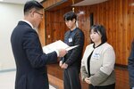 2월 정례조회에 정장을 입고 안경을 낀 남성이 베이지색, 카키색 짧은 양털자켓을 입은 김초원에게 패를 수여하고 있다.
