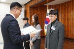 2월 정례조회에 정장을 입고 안경을 낀 남성이 짙은 회색 목티에 조금더 밝은 회색 모직 자켓을 입은 이동준에게 패를 수여하고 있다.